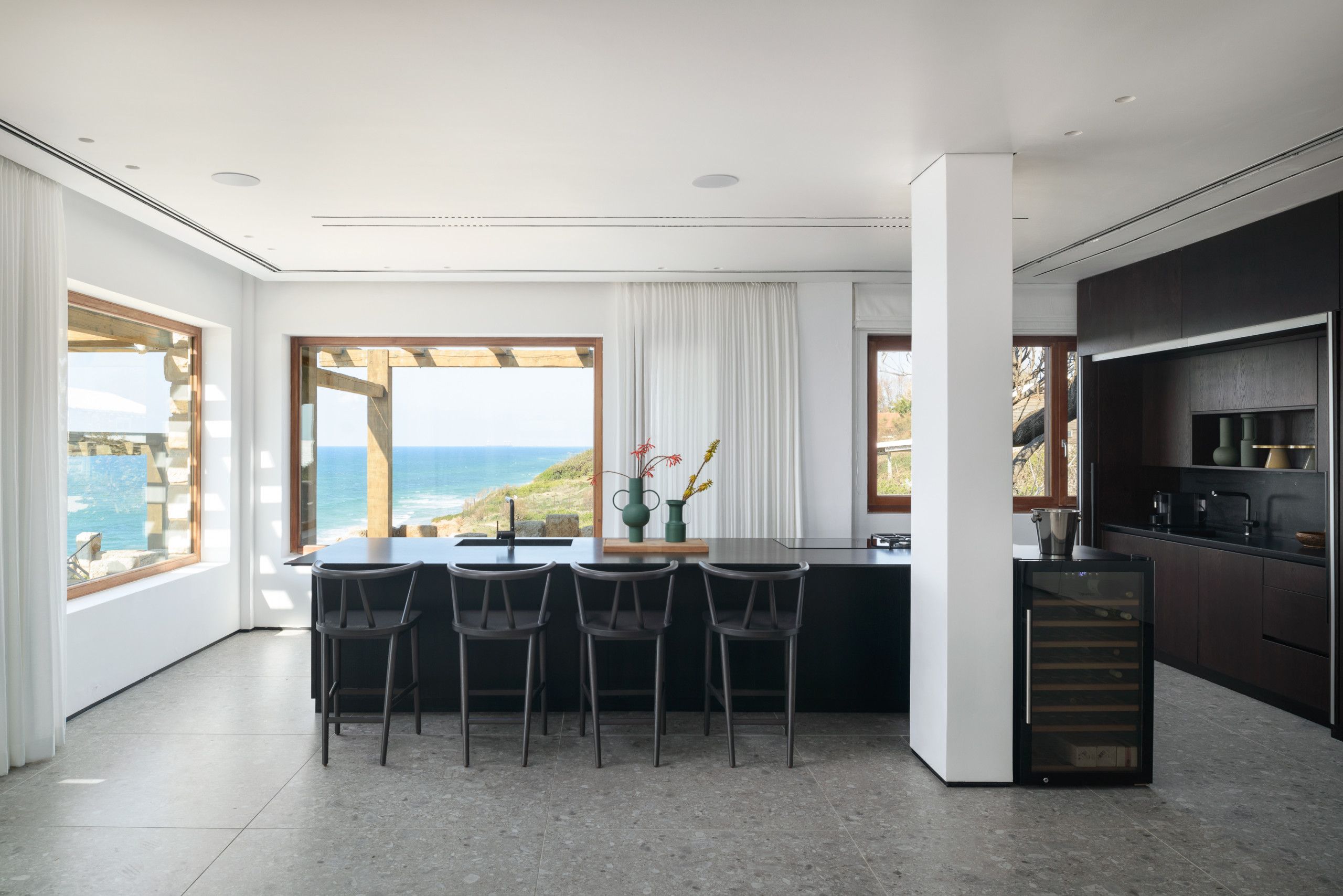 Una cocina moderna con una isla grande, taburetes de bar y vista al océano.