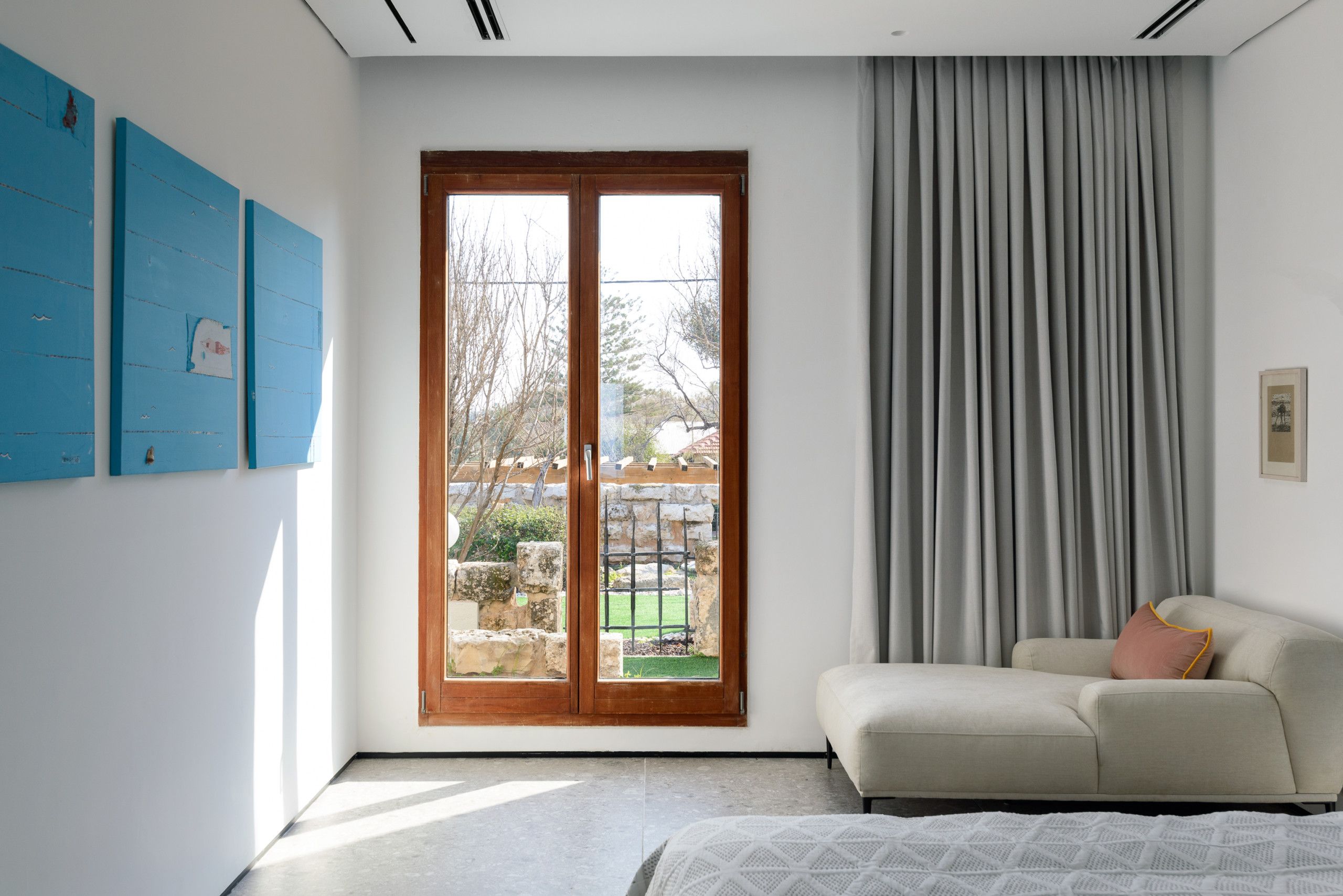 A modern bedroom with a large sliding glass door leading to an outdoor area, a beige sofa, and a bed with a patterned cover.