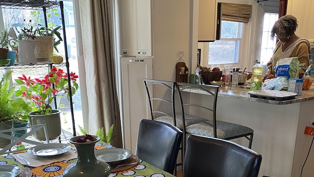 Un comedor con una mesa dispuesta para cuatro, una cocina al fondo y una persona preparando comida.