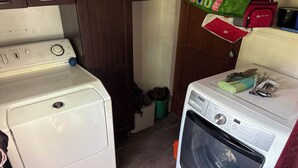 Un área de lavandería con lavadora y secadora de carga frontal, un armario de madera y un bote de basura.