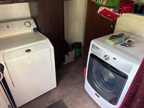 Ein Waschbereich mit einer Frontlader-Waschmaschine und einem Trockner, einem Holzschrank und einem Mülleimer.