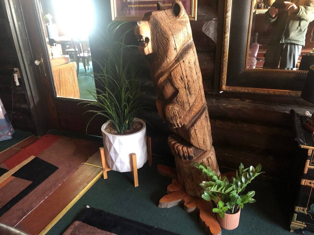 A wooden bear sculpture, a potted plant, and a mirror in a room with a patterned carpet.