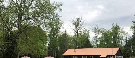 Un chalet avec un toit rouge, entouré d’arbres, et une route goudronnée devant.