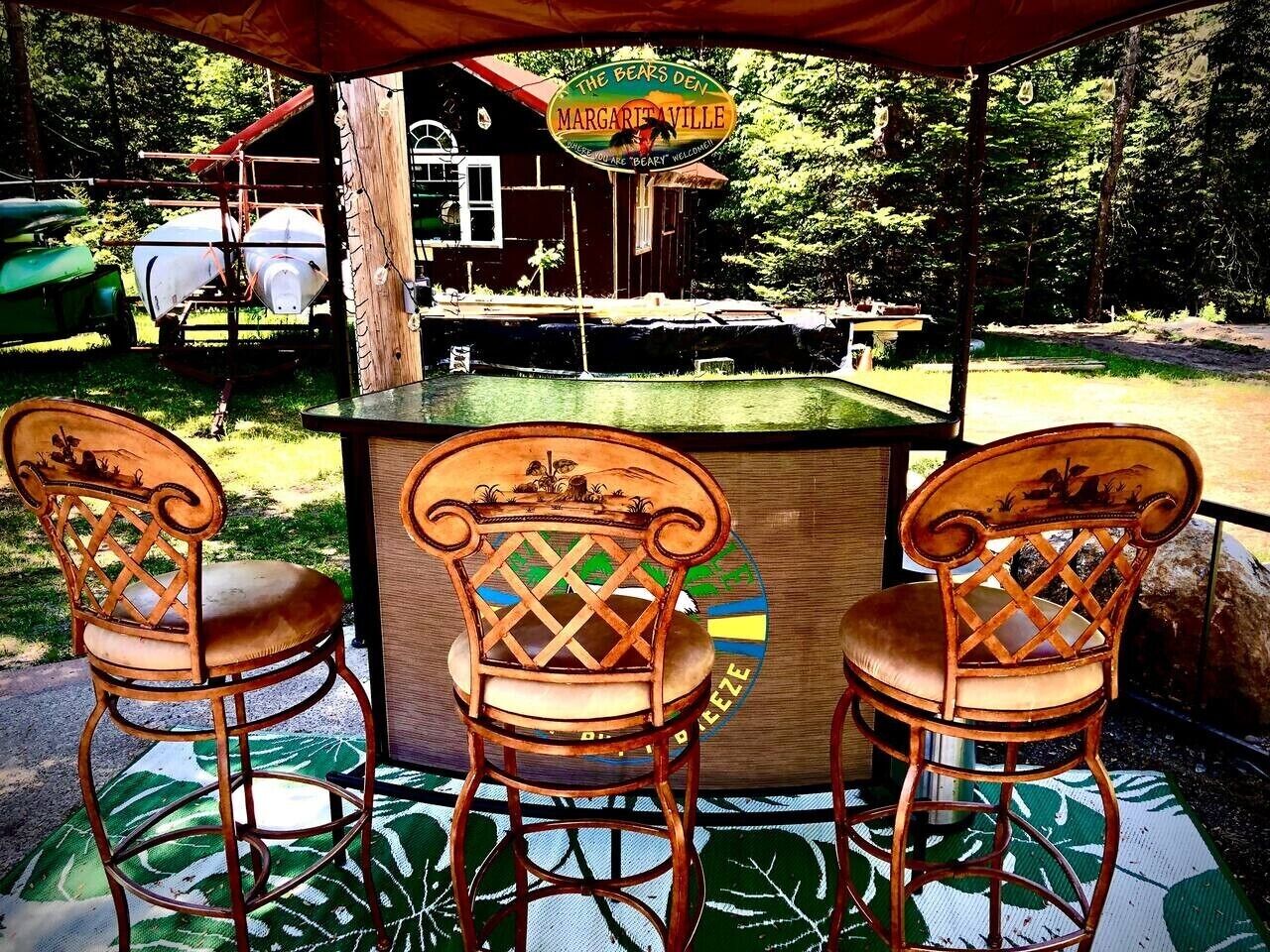 Una barra de madera con tres sillas, un letrero que dice 'The Bears Den Margaritaville' y una casa al fondo.
