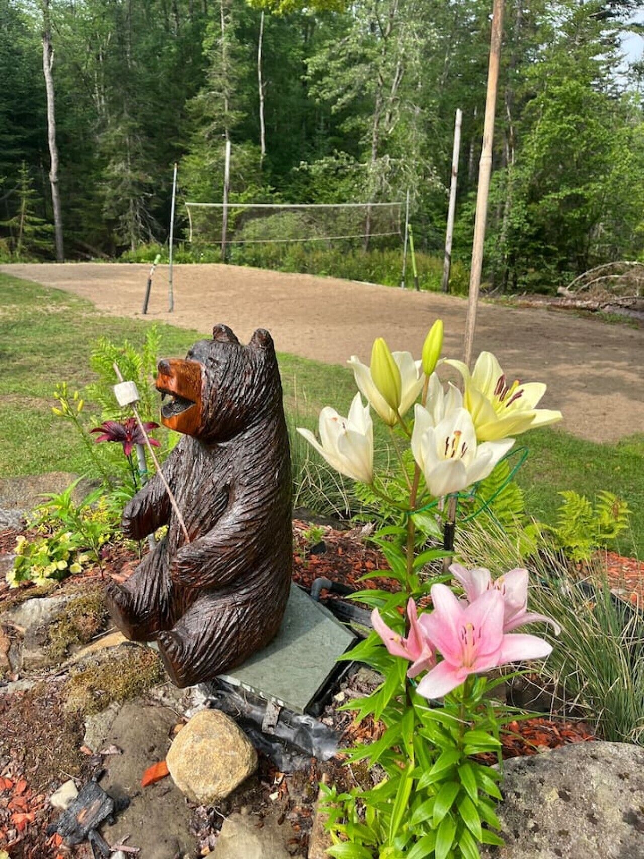 A garden with a bear statue, flowers, and a dirt path.