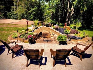Un'area patio con due sedie di legno e un piccolo giardino roccioso con piante e una fontana.