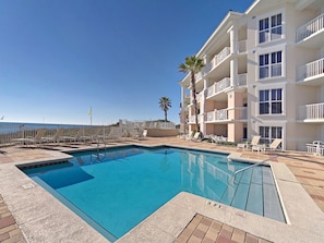 A swimming pool with lounge chairs and a building with balconies.