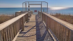 Une promenade en bois menant à une plage, avec une barrière métallique et un panneau rouge.