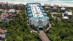 Vue aérienne d’un hôtel situé sur la côte, avec un bâtiment central doté d’un toit végétalisé, entouré d’une végétation luxuriante et de propriétés en bord de mer.