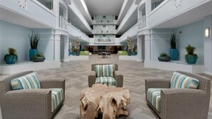 Un vaste atrium à plusieurs niveaux, doté de hauts plafonds et d’un espace central ouvert aménagé avec des coins salon et des plantes en pot.