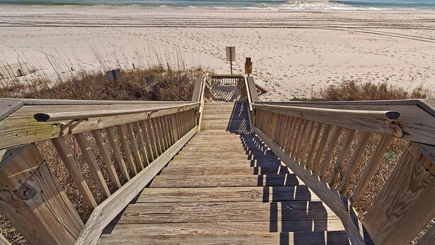Une promenade en bois qui mène à une plage offrant une vue dégagée sur l’océan.