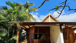 Een houten huis met balkon, omringd door palmbomen en een helderblauwe lucht.