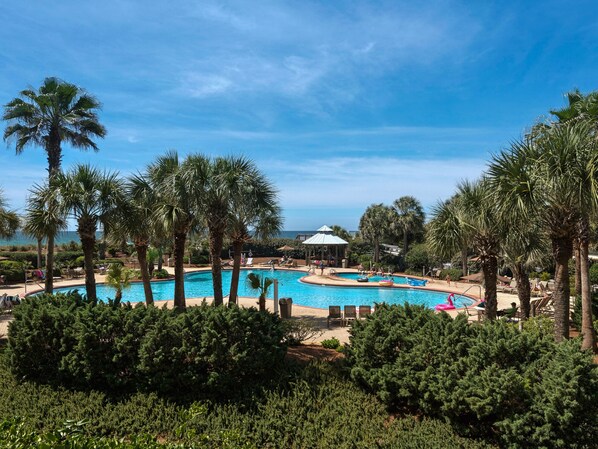 Relax by the resort's oval pool surrounded by lush greenery and palm trees, with lounge chairs and umbrellas nearby.