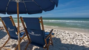 A beach with two blue beach chairs labeled "Crescent" and a blue umbrella. - Beautiful Gulf Front 2 Bedroom Condo in Destin (Miramar Beach)