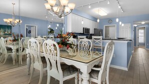 A spacious dining area with a glass-top table, white ornate chairs, and a chandelier. - Beautiful Gulf Front 2 Bedroom Condo in Destin (Miramar Beach)