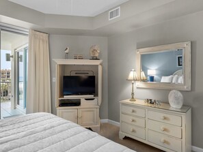 Relax in a spacious room with a large bed, TV, and dresser, offering a view of the outside.
