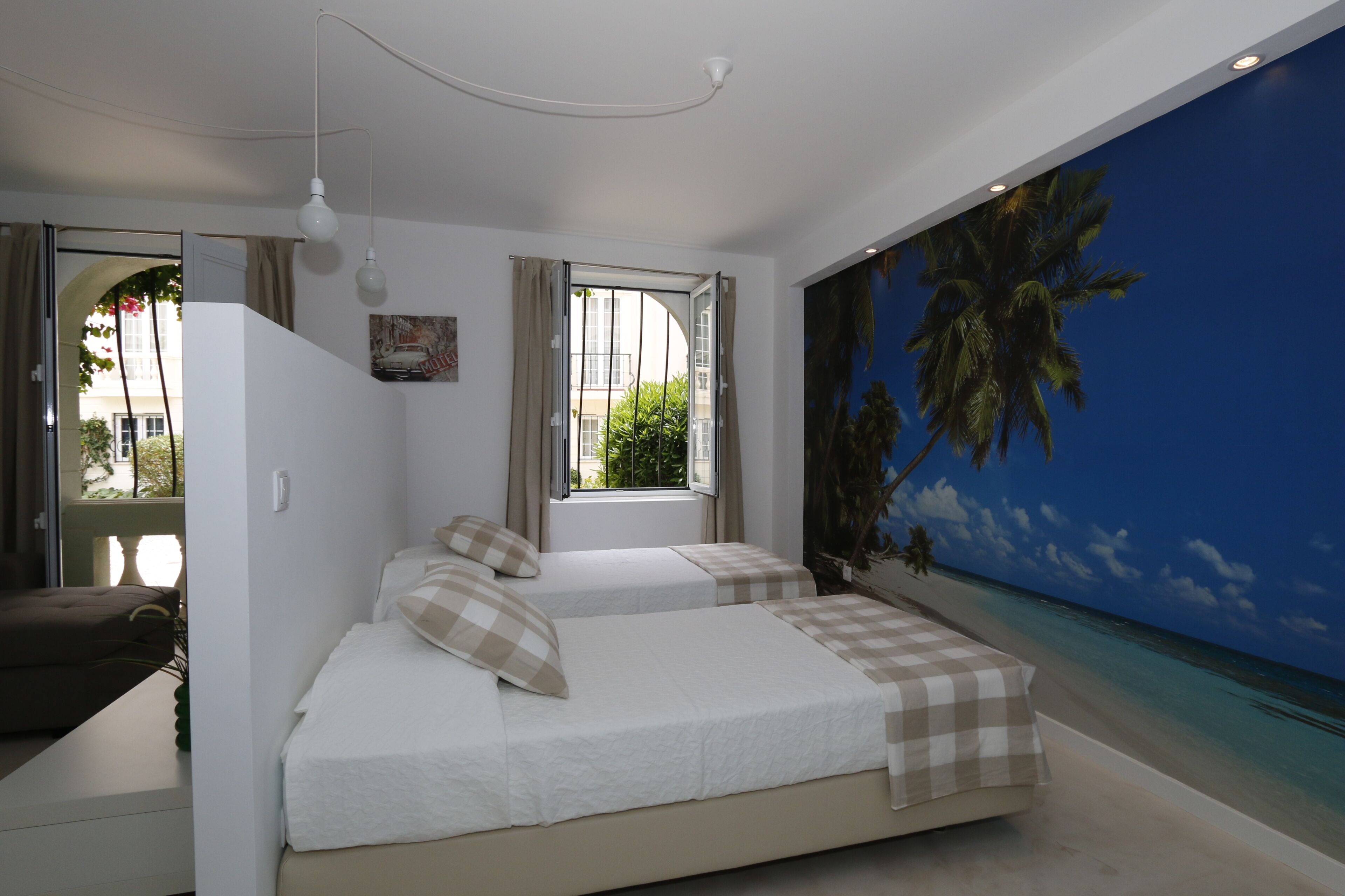 A bedroom with two beds, a large window, and a mural of a beach scene.