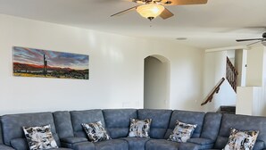 A living room with a sectional sofa, a round coffee table, a ceiling fan, and a painting on the wall. - 6br3ba with pool & jacuzzi (Glendale)