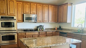 A modern kitchen with wooden cabinets, stainless steel appliances, granite countertops, and a central island with stools. - 6br3ba with pool & jacuzzi (Glendale)