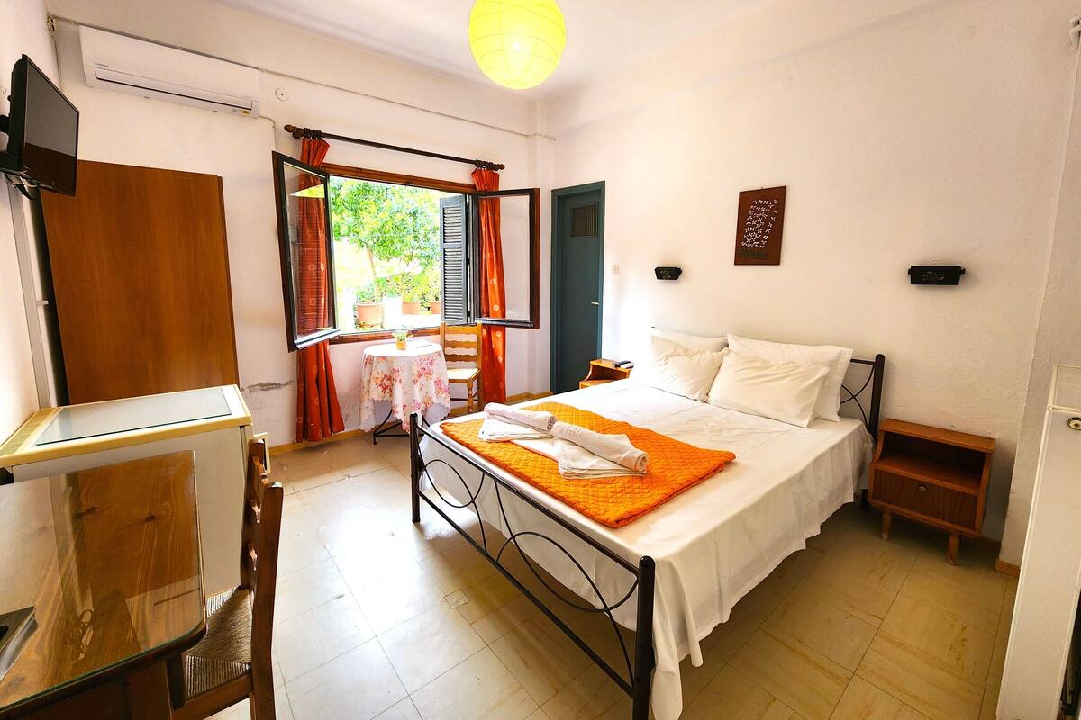 Een slaapkamer met een bed, een bureau, een stoel, een raam met gordijnen en een hanglamp.