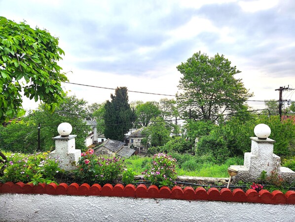 Un jardín con un borde rojo, un árbol alto y una estructura de piedra con un remate esférico.