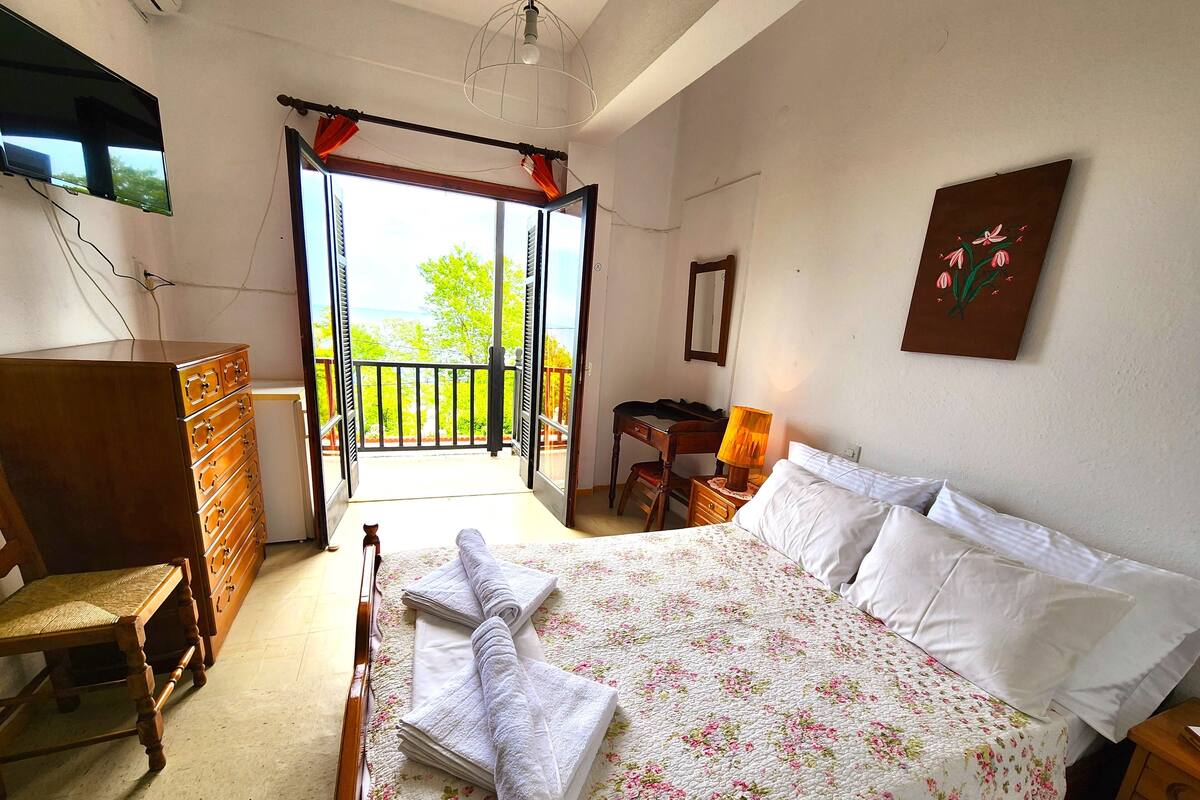 Een slaapkamer met een bed, een dressoir, een bureau en een balkon.