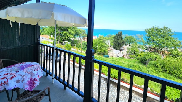 Un balcón con una sombrilla blanca, una mesa con mantel floreado y vistas al mar y la vegetación.