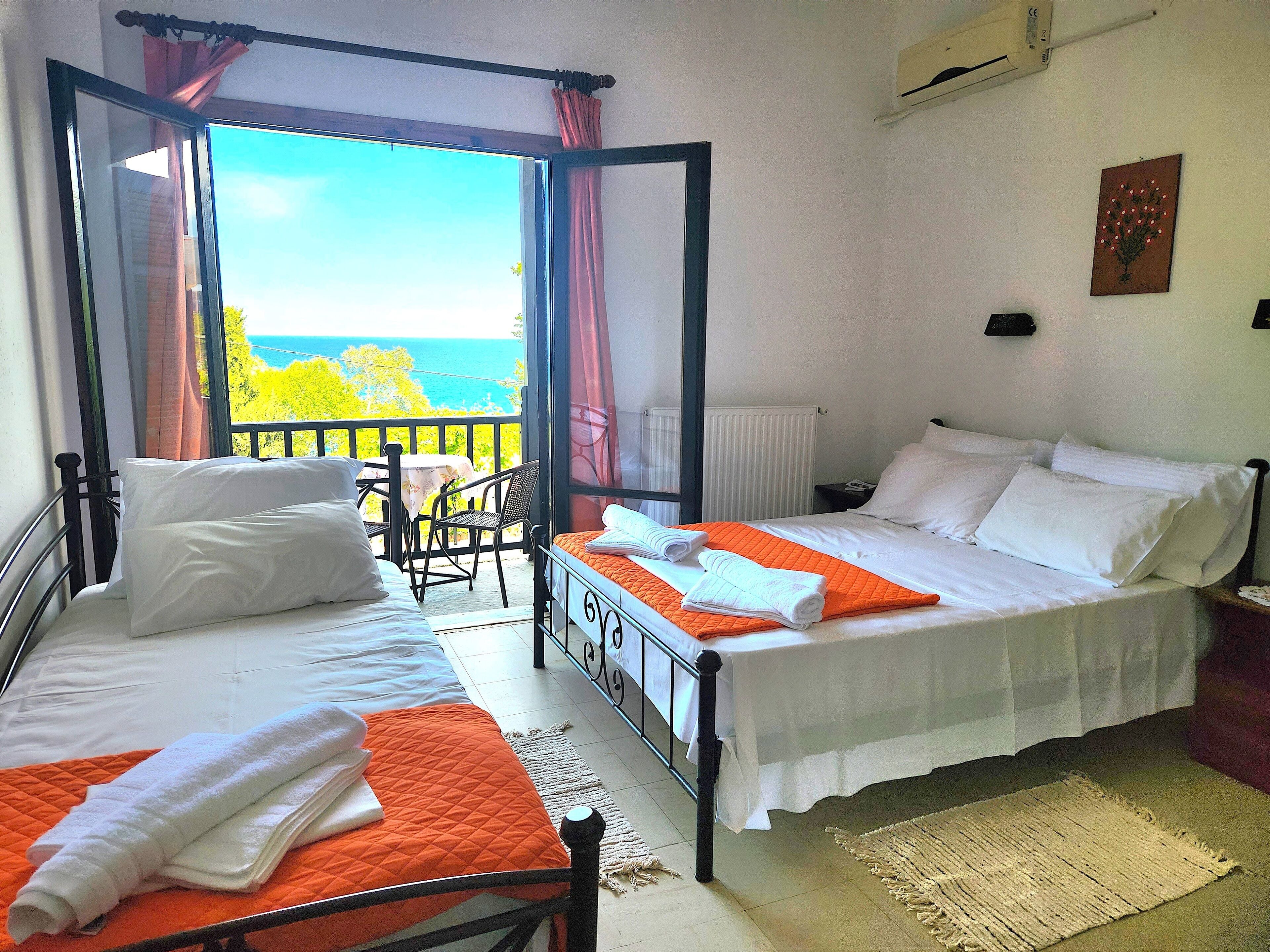 A room with two beds, a balcony with a view of the sea, and a table with chairs.