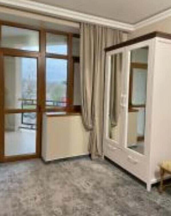 A room with a large sliding glass door leading to a balcony, a white wardrobe, and a carpeted floor.