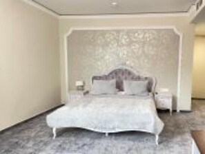 A bedroom with a large bed, a nightstand, and a wall with a floral pattern.