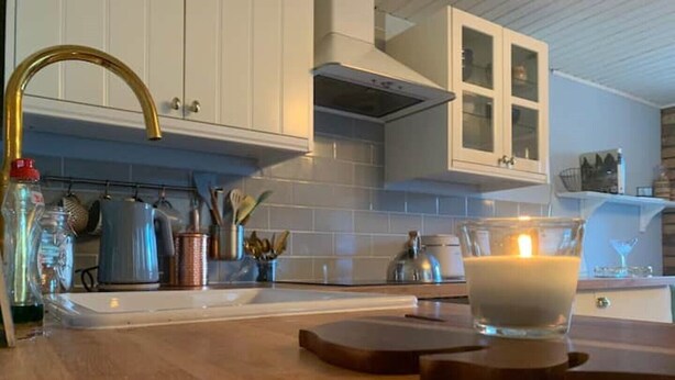 Een keuken met witte kastjes, een roestvrijstalen spoelbak en een brandende kaars op het aanrecht.