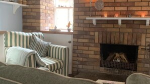 Een gezellige woonkamer met een metselwerk schoorsteen, een gestreepte fauteuil en een bank.