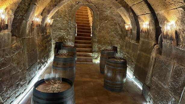 A stone-walled corridor with wooden barrels and wine glasses, leading to a staircase. - CASA PEQUE (Laguardia)