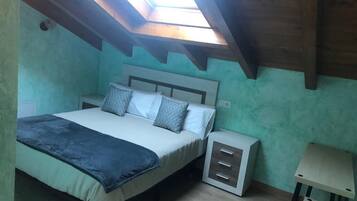 A bedroom with a skylight, a bed with pillows, a bedside table, and a small desk.