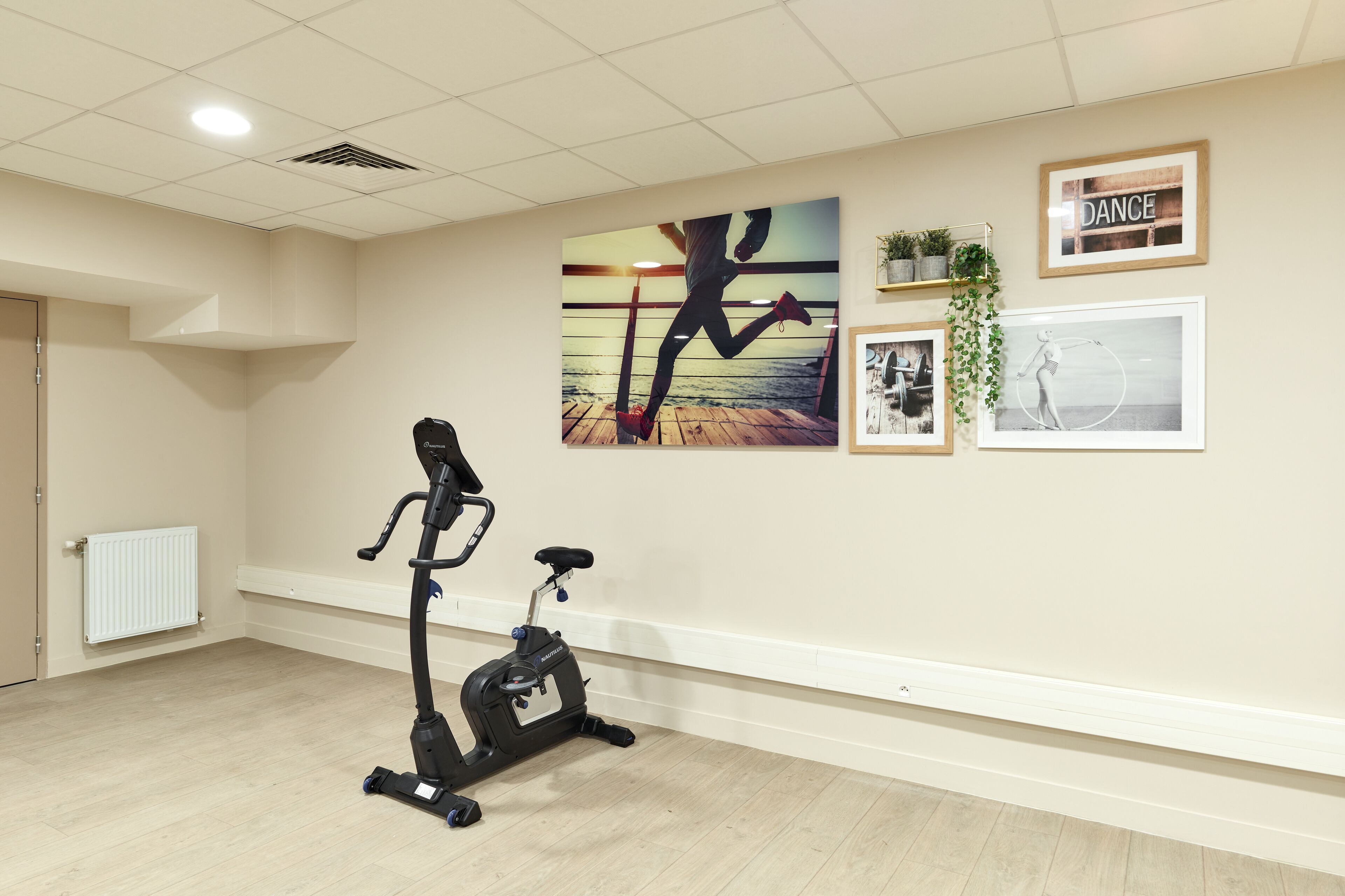 A room with a stationary bike, a radiator, and wall art including a 'DANCE' sign.
