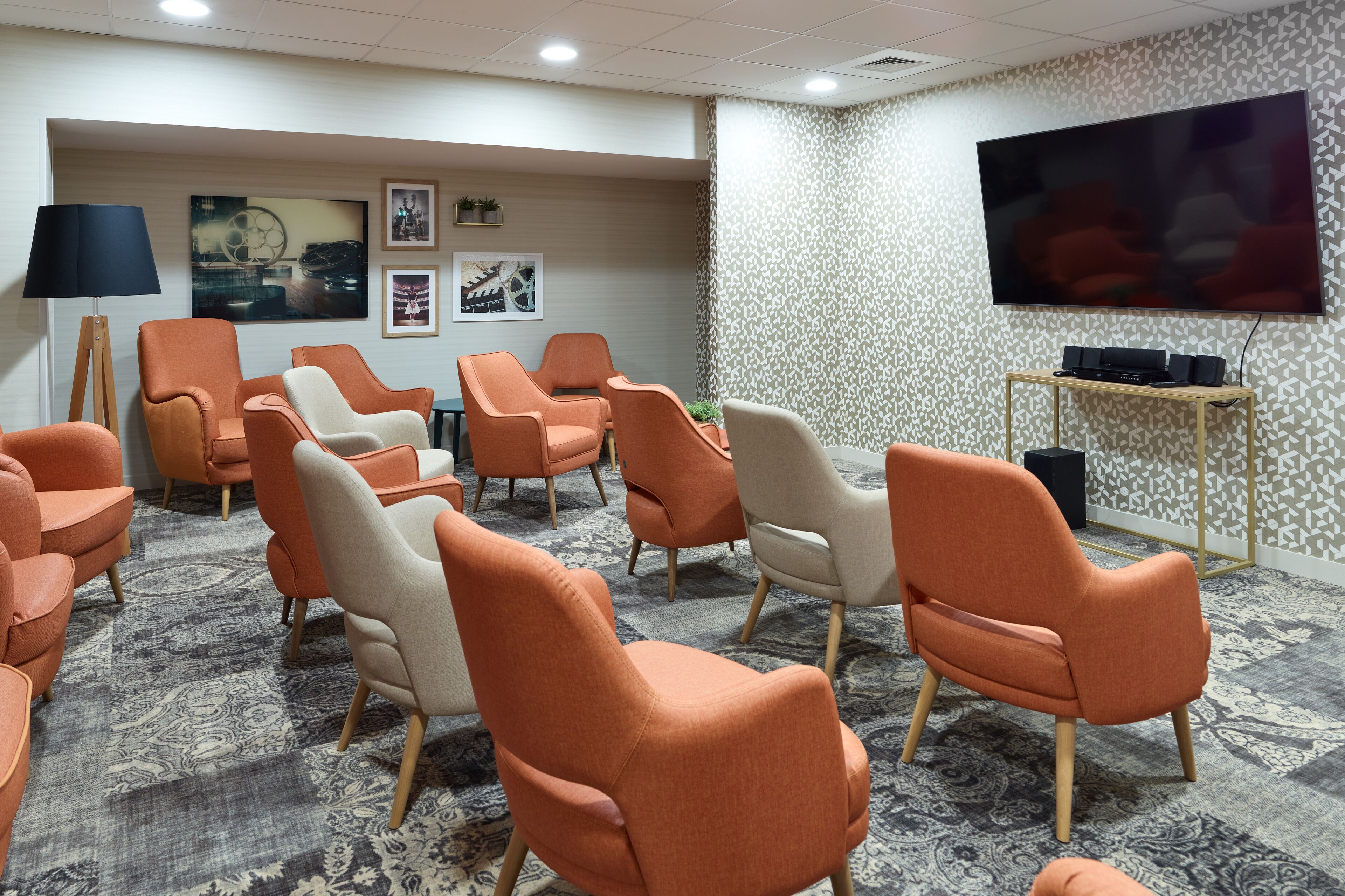 A conference room with orange and white chairs, a large flat-screen TV, and a patterned carpet.