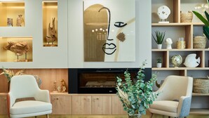 Una sala de estar moderna con chimenea, dos sillones, una mesa de centro y varios objetos decorativos en estantes y paredes.