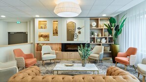 Un vestíbulo de hotel moderno con una zona de estar central, una chimenea y varios objetos decorativos.