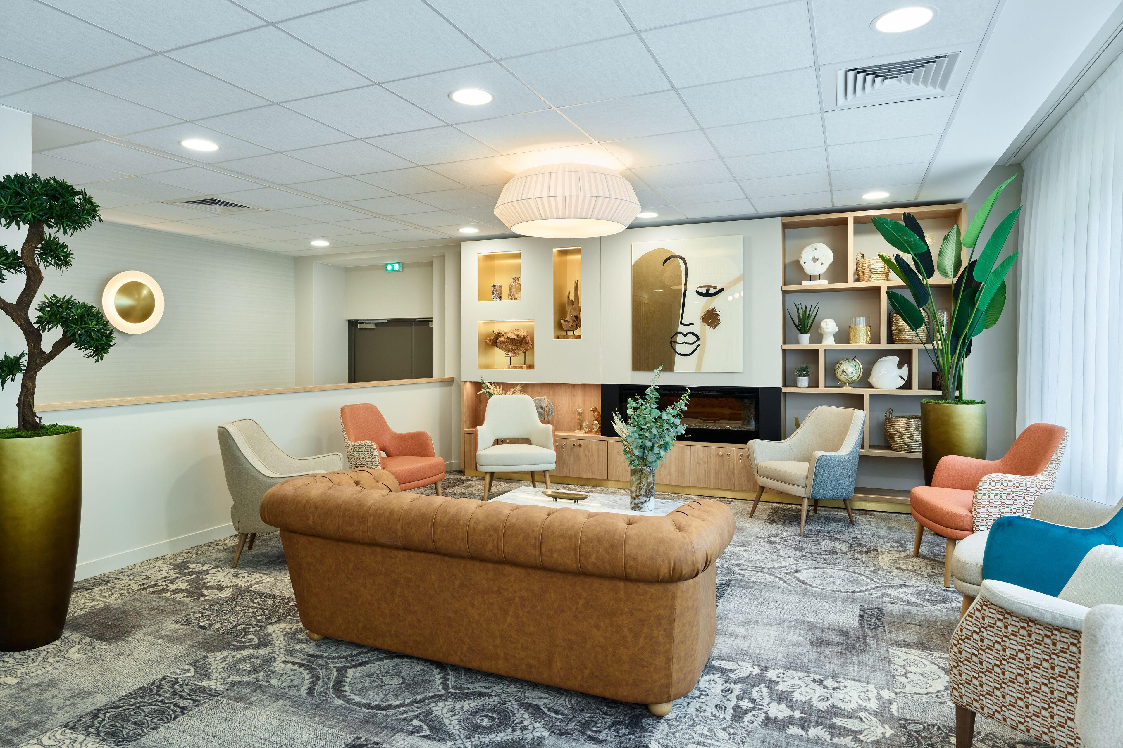 A modern lobby with a brown sofa, white and orange chairs, a large potted plant, and a television.