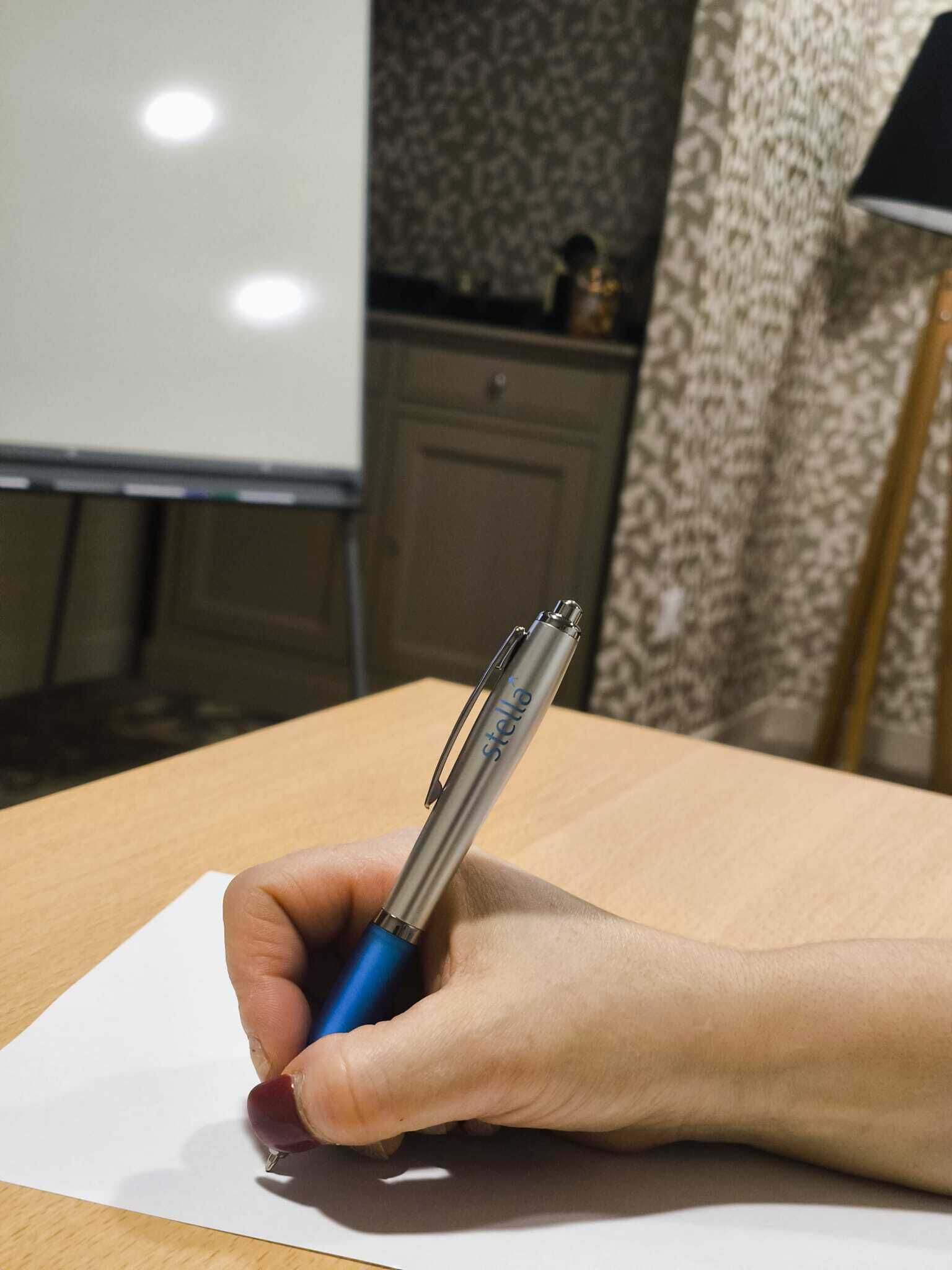 Uma mão segurando uma caneta, escrevendo em um papel.