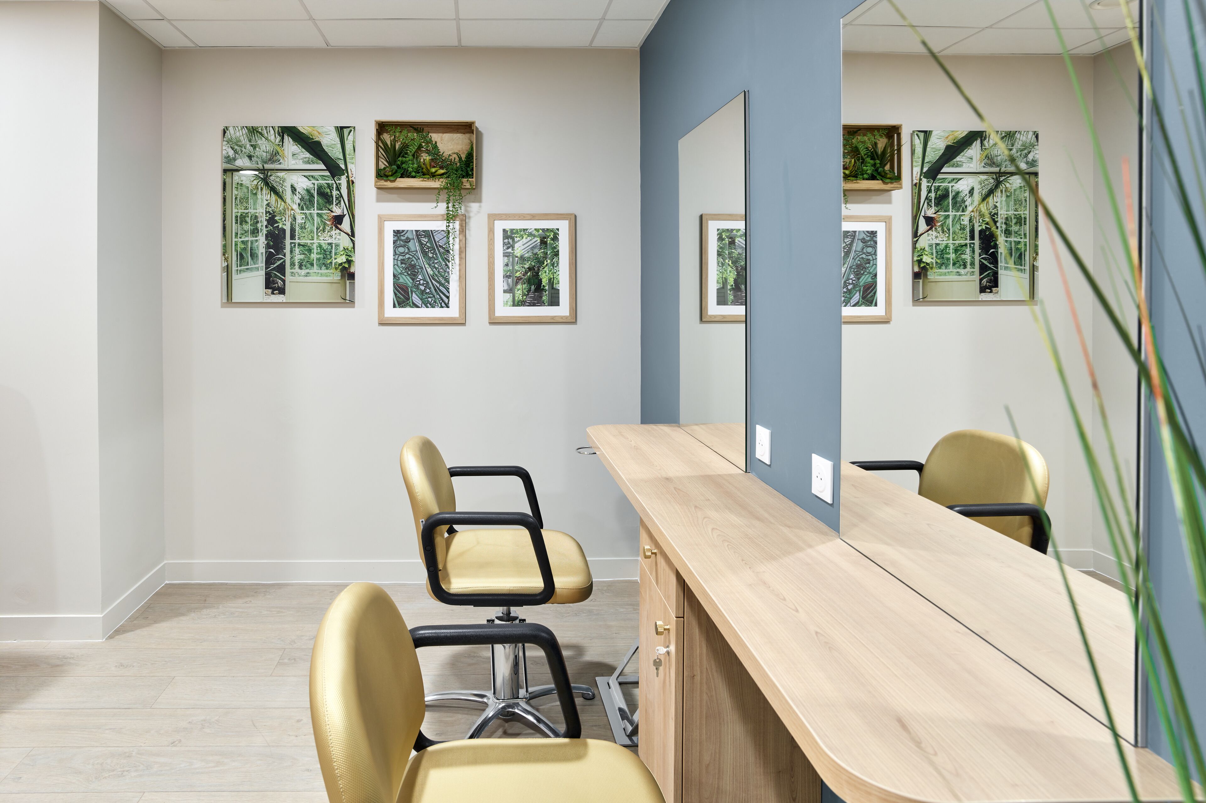 Une chambre moderne avec un bureau en bois, deux chaises et des reproductions encadrées de motifs botaniques accrochées au mur.