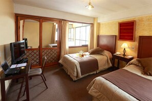 A hotel room with two beds, a desk with a laptop, a TV, and a window with curtains. - El Puma (Cusco)