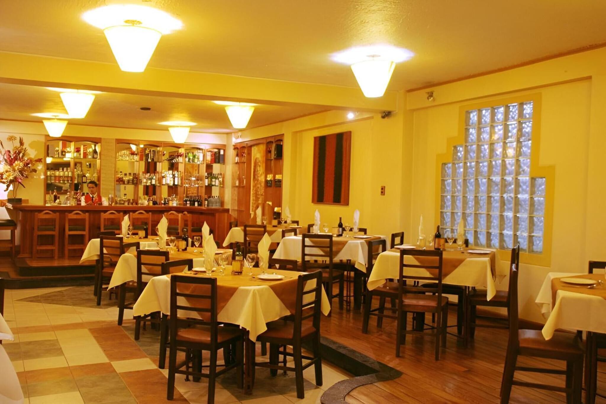 Um restaurante com várias mesas e cadeiras, uma área de bar e grandes janelas.