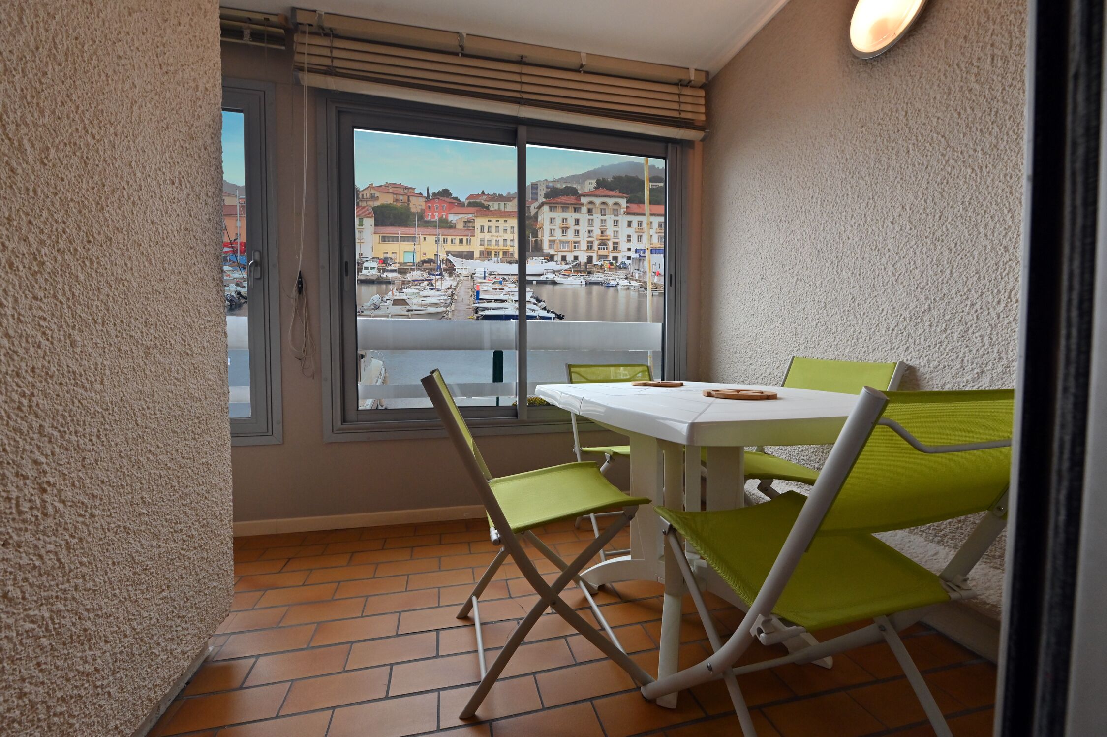 Un balcon avec une table et des chaises, une vue sur une marina avec des bateaux, et un paysage urbain en arrière-plan.