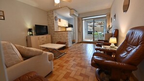 Ein Wohnzimmer mit einer Couch, einem braunen Ledersessel, einem Fernseher und einem Esstisch.