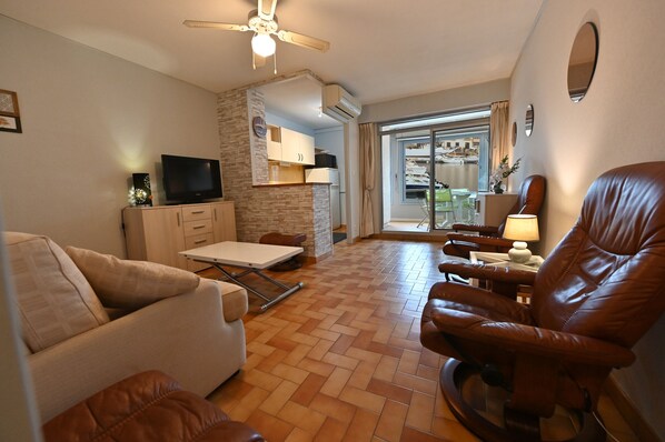 A living room with a sofa, a brown leather chair, a TV, and a dining table.
