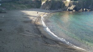 Ein Strand mit klarem Wasser, Kieselsteinen und einer steilen Klippe.
