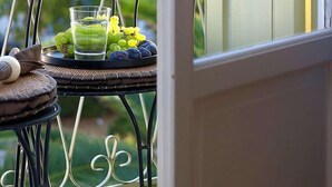 A balcony with a table holding a glass of water and grapes, and a door with shutters. - Family Latini Hotel (Nafplio)