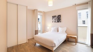 A bedroom with a bed, bedside tables, a nightstand, a sliding door, and a view of the outside. - Zenao Appart'hôtels Montreuil (Montreuil)