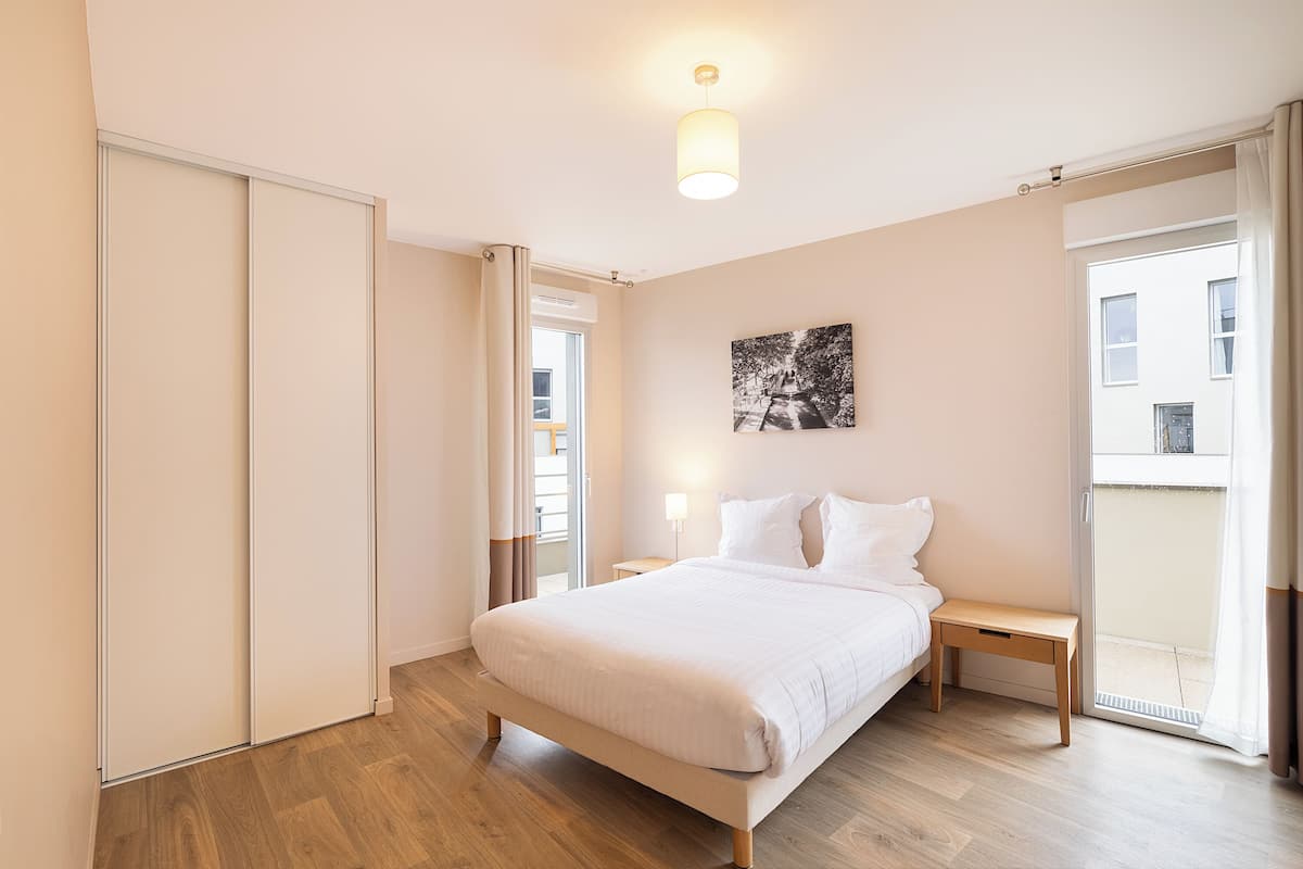 A bedroom with a bed, bedside tables, a nightstand, a sliding door, and a view of the outside.